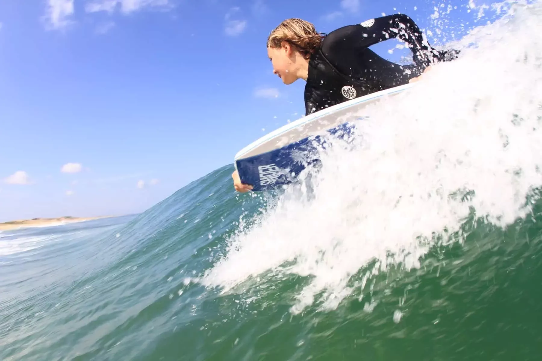 Jovem surfista em prancha esquerda a vencer a onda, com água a espumar ao redor.